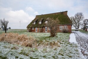 Une maison traditionnelle en briques, avec un toit à forte pente, un petit jardin et une allée pavée.