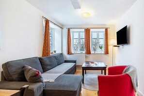 Un salon avec un canapé, un fauteuil rouge, une table et un téléviseur fixé au mur.