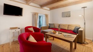 Un salon avec une télévision, des fauteuils rouges, un canapé, une table basse, un lampadaire et une fenêtre avec des rideaux.