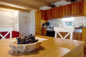 Una mesa de madera con un bol de uvas y una silla blanca en una cocina con armarios de madera y encimera blanca.