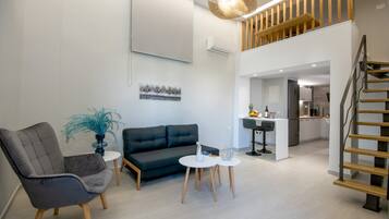 Een moderne woonkamer met een bank, stoelen, een salontafel en een trap naar een hoger gelegen verdieping.