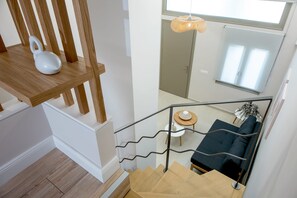 Eine Treppe mit Holzgeländer und Metallreling, die zu einem dunkelgrauen Sofa und einem kleinen runden Tisch mit einem weißen Gegenstand darauf führt.