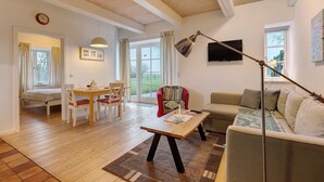 A living room with a wooden floor, a sofa, a table, a TV, and a window.