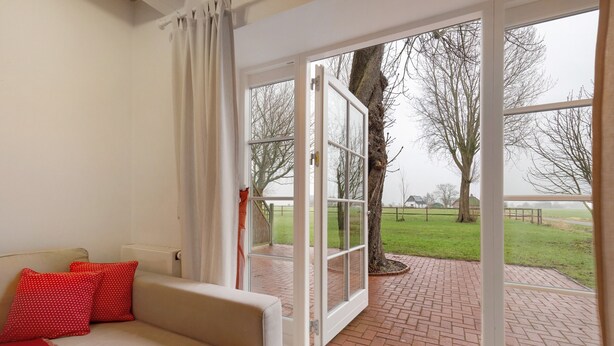 A room with a sofa, red pillows, and a view of a brick pathway and trees outside.