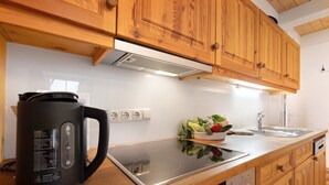A kitchen with wooden cabinets, a black electric kettle, a stainless steel induction cooktop, and a dishwasher.
