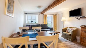 Una sala de estar acogedora con sofá, mesa de comedor, sillas, televisor y ventana con cortinas.