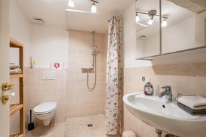 A bathroom with a toilet, shower, sink, and a mirror.