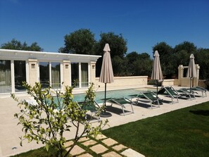 A pool area with lounge chairs and umbrellas, a modern building with large windows, and a well-maintained lawn.