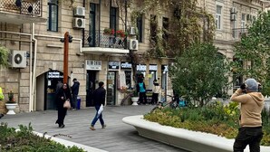 Una plaza pública con un edificio que tiene varios balcones, unidades de aire acondicionado y una variedad de tiendas, incluyendo una cafetería y un mercado.