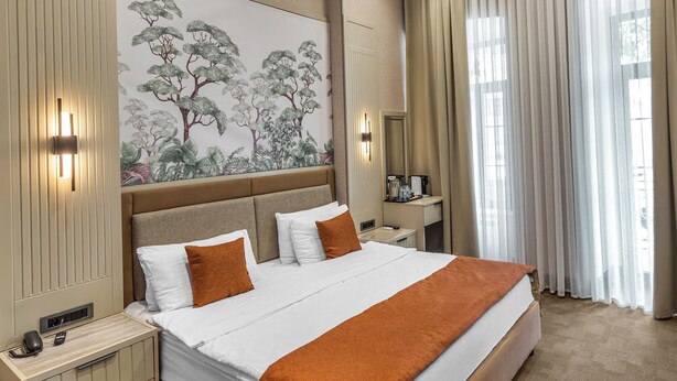 Una habitación de hotel moderna con una cama grande, una mesita de noche, un escritorio y un ventanal con cortinas.