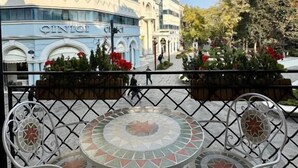 Un edificio con el nombre 'Qinai' en su fachada, un área de estar al aire libre con baldosas y un suelo estampado, y un cielo despejado.