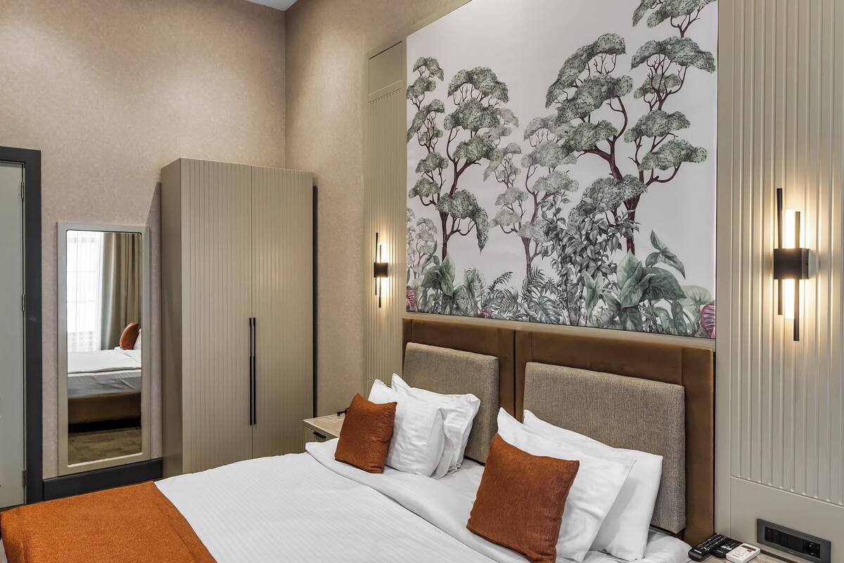 Una habitación de hotel moderna con una cama grande, un armario, una mesita de noche y una pared con un mural de temática natural.