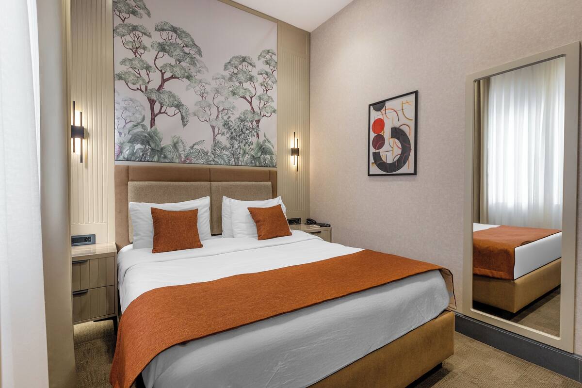 Una habitación de hotel con una cama grande, una mesita de noche, una lámpara de pared, un cuadro y un espejo.