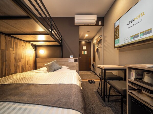 Una habitación de hotel con cama, escritorio y televisor montado en la pared.