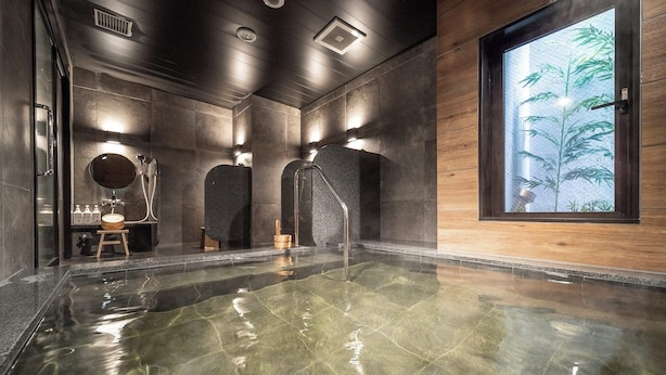 A modern spa with a large indoor pool, wooden accents, and a view of bamboo through a window. - Super Hotel Premier Namba Shinsaibashi Natural Hot Spring (Osaka)