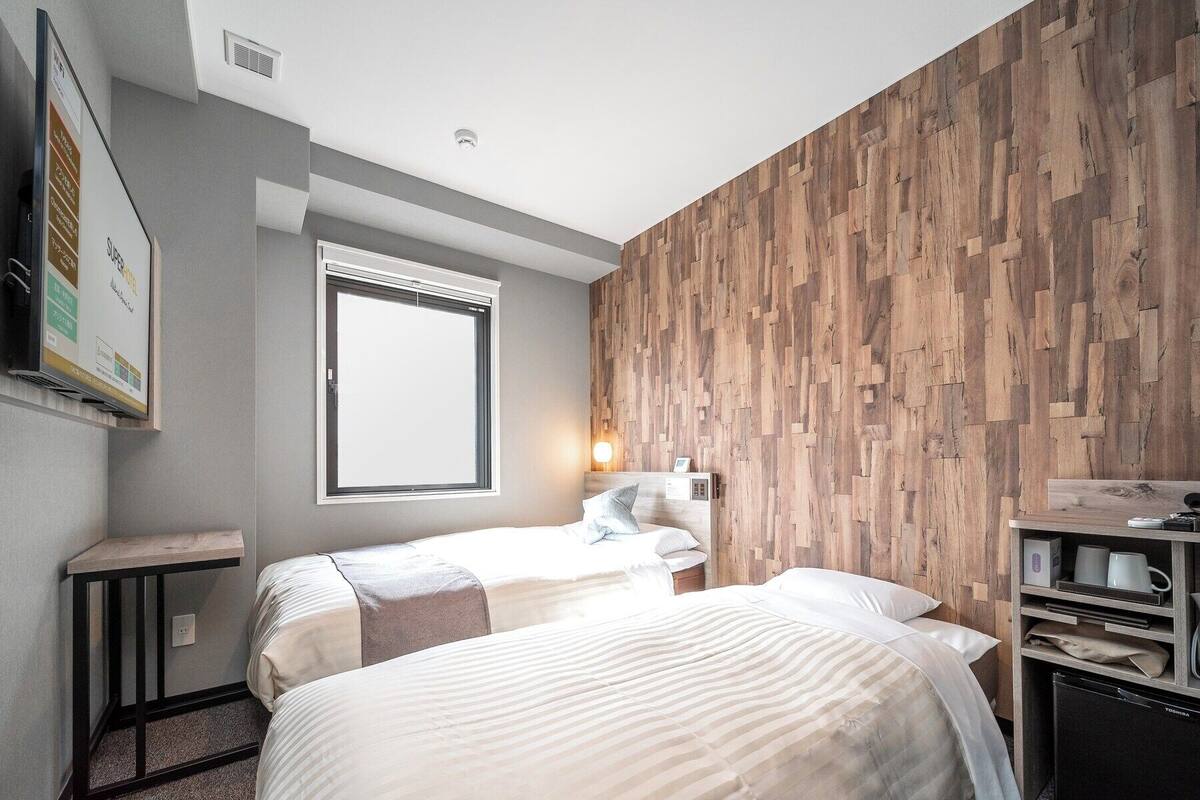 Habitació d'hotel moderna amb dos llits, un mur decoratiu de fusta, un taulell petit i televisió integrada.