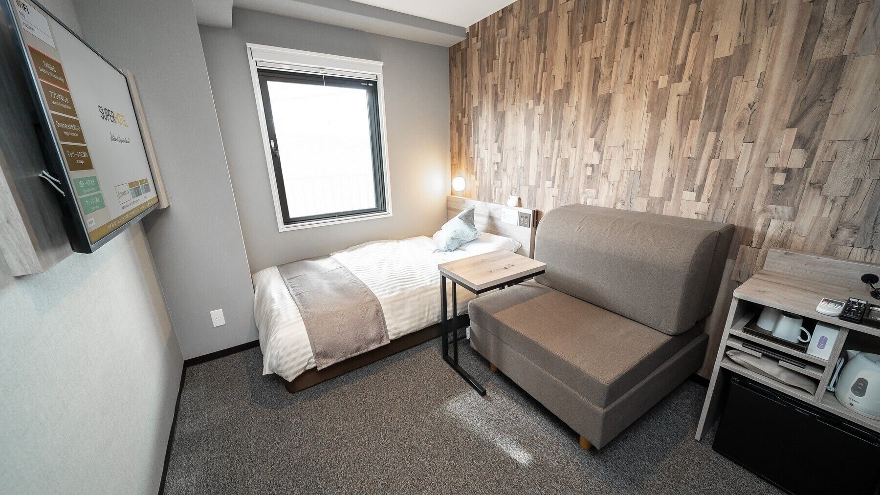 Habitación de hotel pequeña con cama, sofá, una mesita, escritorio y cocina integrada.