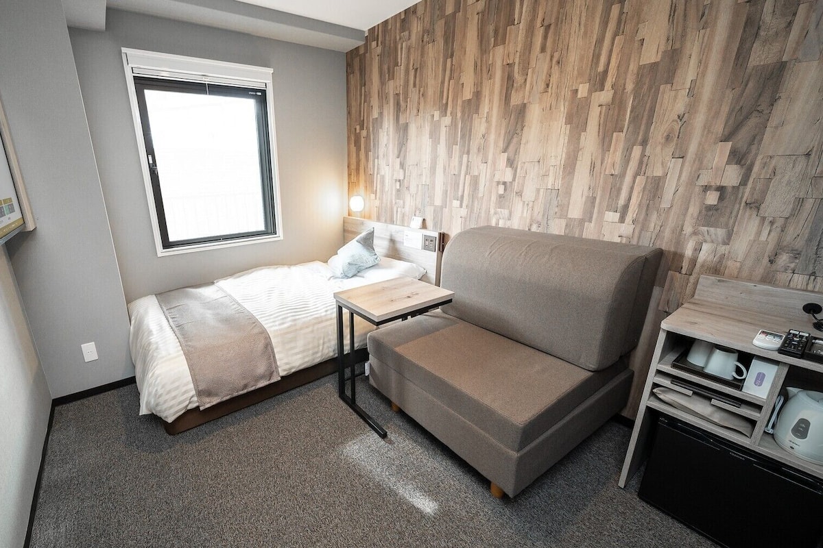 Habitación de hotel pequeña con cama, sofá, una mesita, escritorio y cocina integrada.