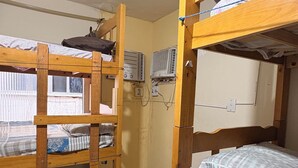 A dormitory room with bunk beds, a window, and an air conditioning unit.