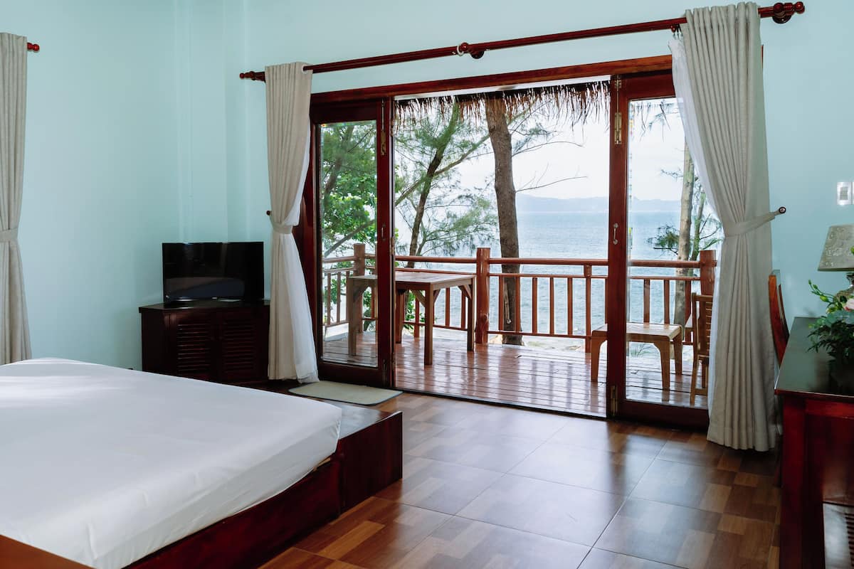A bedroom with a bed, a TV, and a view of the sea through a glass door.