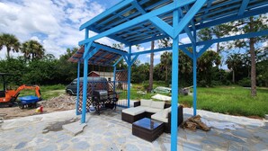 Un espace extérieur abrité, doté d’une structure métallique bleue, d’un sol en pierre et de mobilier d’extérieur.