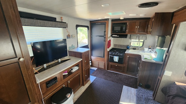 Une cuisine compacte pour camping-car, équipée d’une cuisinière, d’un four à micro-ondes, d’un évier et d’un téléviseur.