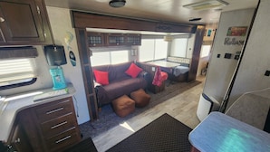 Un intérieur de camping-car compact comprenant un coin cuisine, un espace salon avec des coussins et une petite table à manger.