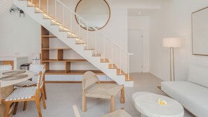 A modern living room with a staircase, a round mirror, a sofa, a coffee table, and a dining area with chairs and a table. - A.K.A Cemagi Townhouse (Cemagi)