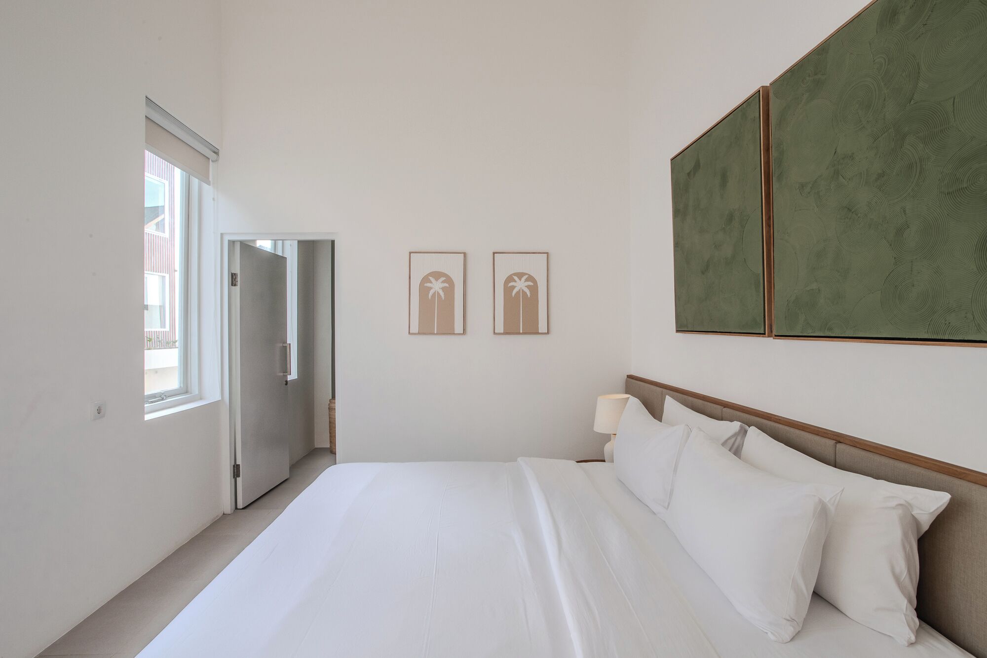Habitación de hotel con una cama, una mesita de noche, una ventana y dos obras de arte colgadas en la pared.