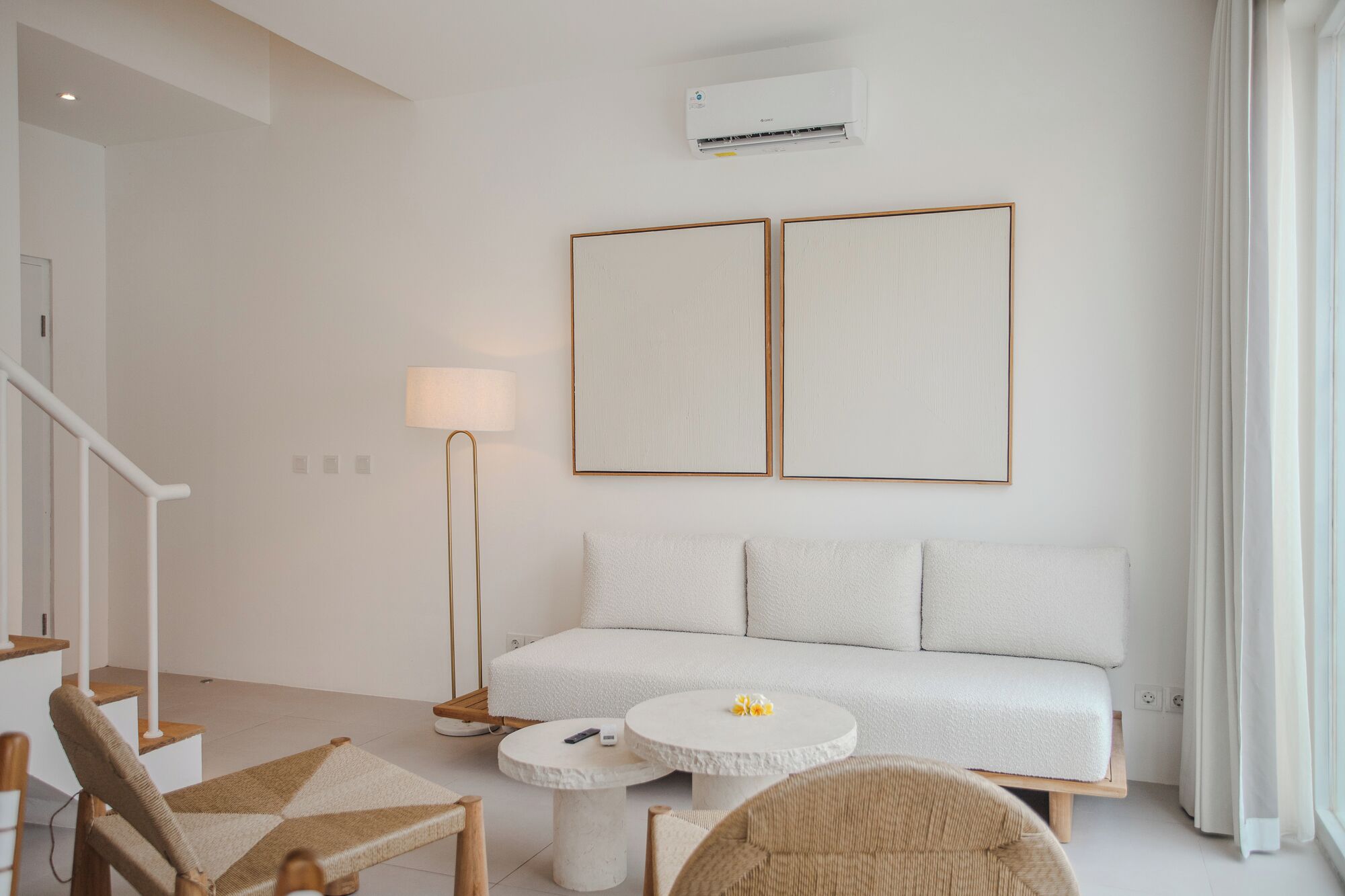 Una sala de estar moderna con un sofá blanco, dos cuadros enmarcados, una lámpara de pie y una mesa de centro redonda.