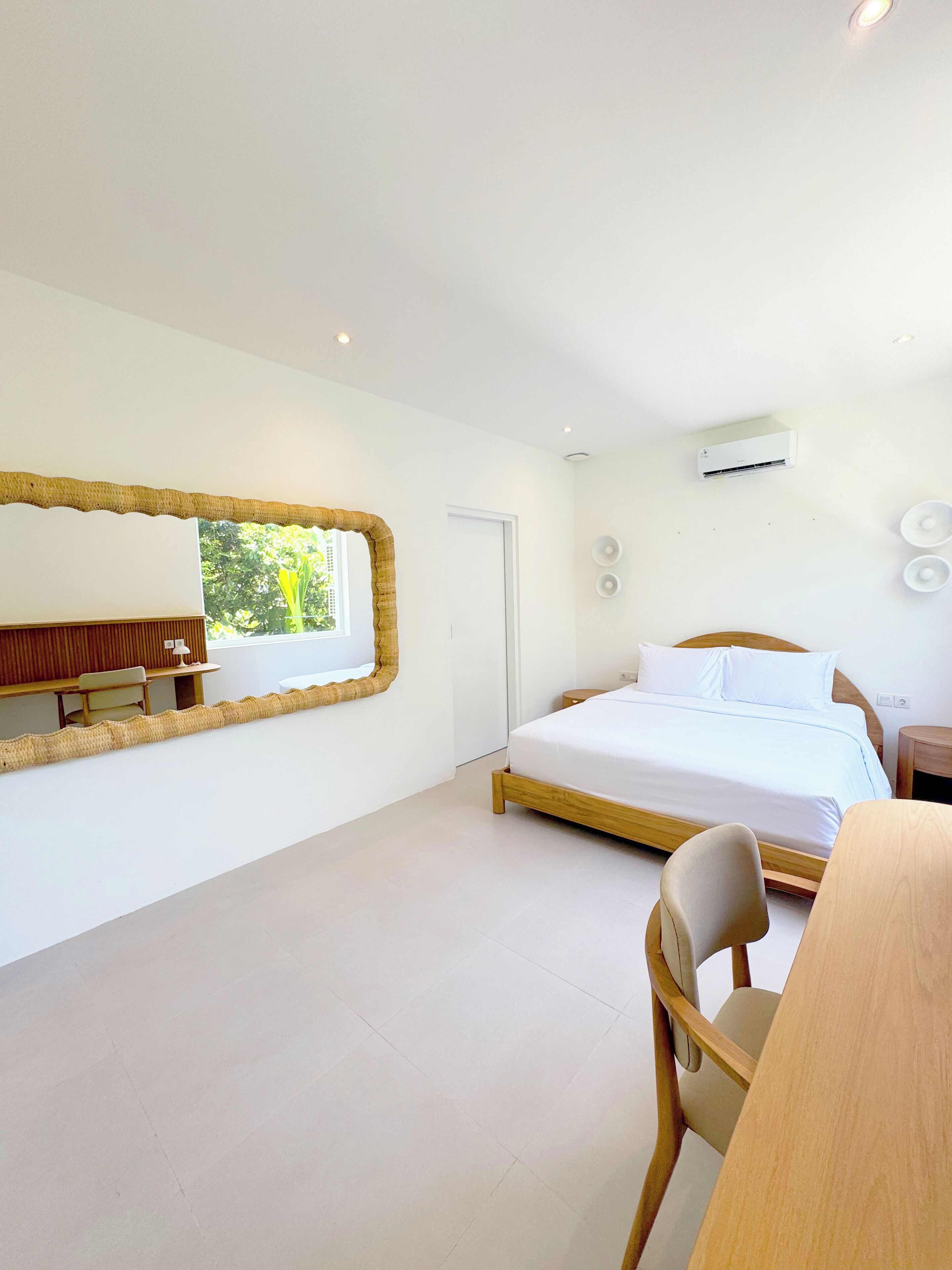 A modern bedroom with a large bed, a wooden desk, a chair, and a large mirror.