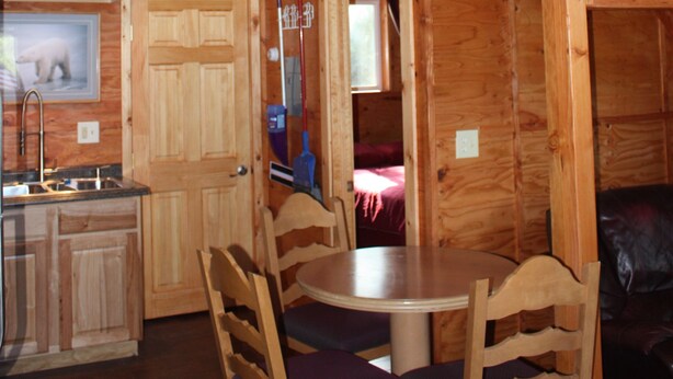 Interior de una cabaña de madera con comedor, cocina y un dormitorio en lo alto.