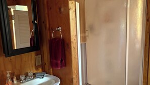 A wooden bathroom with a white sink, a mirror, a towel rack, and a shower enclosure.