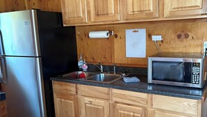A kitchen with wooden cabinets, a stainless steel refrigerator, a microwave, and a sink.