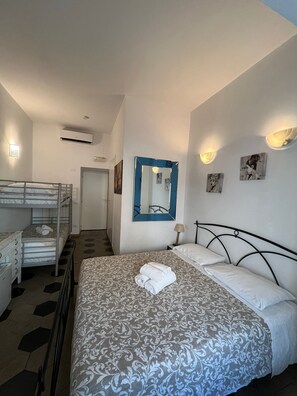 A hotel room with a bunk bed, a large bed with a patterned bedspread, a mirror, wall-mounted lights, and artwork. - Deluxe Vatican (Rome)