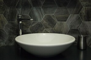 A modern bathroom with a large white sink, a sleek faucet, and a metallic container on the countertop. The walls are covered with hexagonal dark tiles. - Deluxe Vatican (Rome)