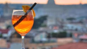 Ein Cocktailglas mit Zitronenscheibe und Trinkhalm vor einer Stadtkulisse.