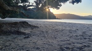 En strand med en klippefremspring, roligt vand og fjerne bjerge under en klar himmel.