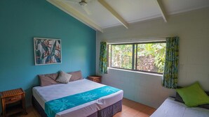 A bedroom with a bed, a window with curtains, a ceiling fan, and a wall painting. - Muri Lagoon Lodge (Rarotonga)