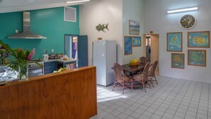 A kitchen with a dining area, white tiled floor, and wall-mounted artwork. - Muri Lagoon Lodge (Rarotonga)