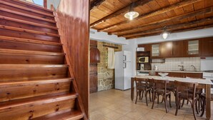 Escada de madeira leva a uma cozinha com paredes de pedra, uma mesa de jantar e cadeiras de madeira.