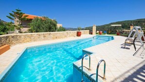 Piscina com águas azuis cristalinas, rodeada por um muro de pedra e um deck ladrilhado.
