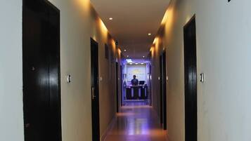 A hotel hallway with a reception desk at the end, featuring a modern design with recessed lighting and a tiled floor.