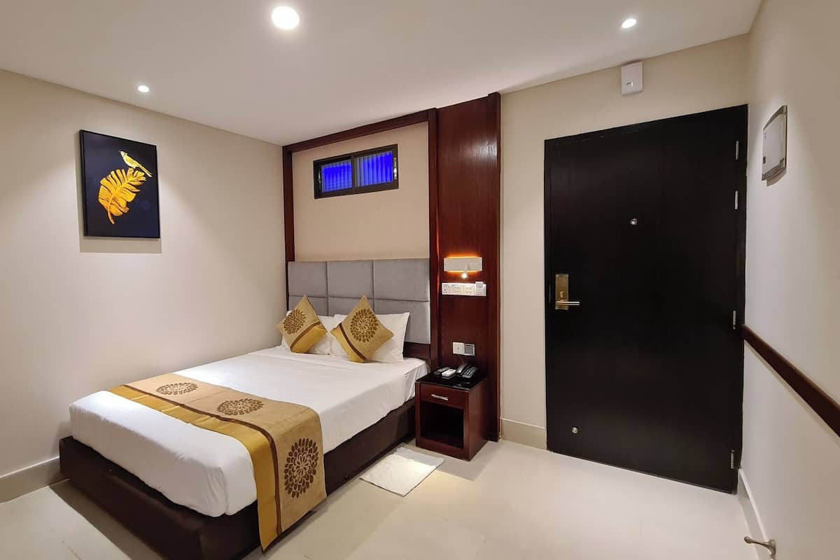 A hotel room with a bed, bedside table, nightstand, and a door.