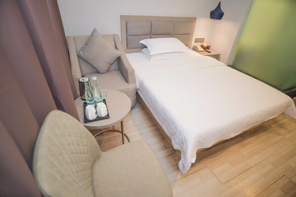 Una habitación de hotel con cama, sofá, una pequeña mesa redonda con botellas y una silla.