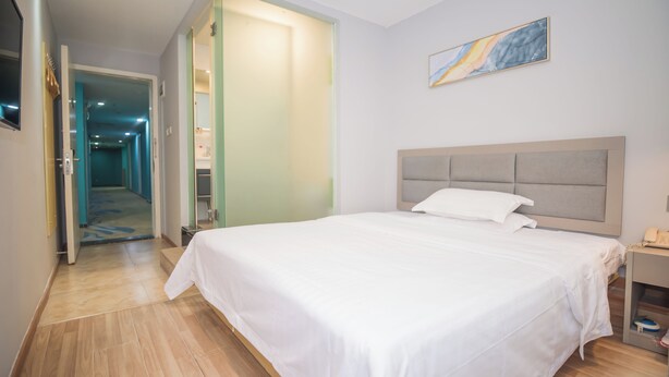 A hotel room with a large bed, a bedside table with a lamp, a painting on the wall, and a hallway leading to another room. - yimimopeichengdian (Guangzhou)