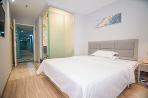 Ein Hotelzimmer mit einem großen Bett, einem Nachttisch mit Lampe, einem Bild an der Wand und einem Gang zu einem weiteren Zimmer.