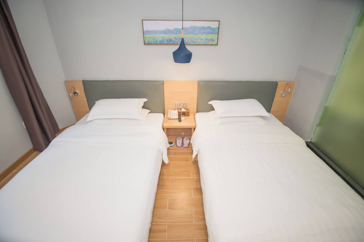 A double bed room with a wooden headboard, a bedside table with a lamp, and a painting on the wall.