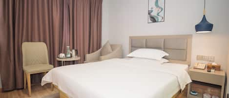 A hotel room with a large bed, a chair, a small table with a kettle, a nightstand with a lamp, and a painting on the wall.