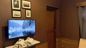 A room with a flat-screen TV on a white stand, a wooden door, and a brown wall with framed pictures. - Hotel Jafson Accommodates (Srinagar)